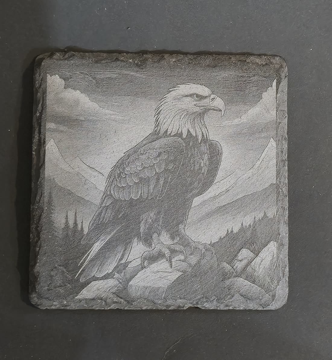 Slate coaster engraved with a bald eagle perched on rocks in front of mountains