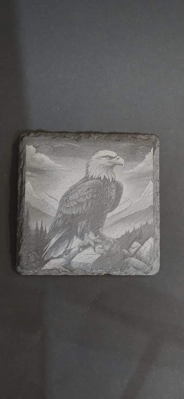 Slate coaster engraved with a bald eagle perched on rocks in front of mountains